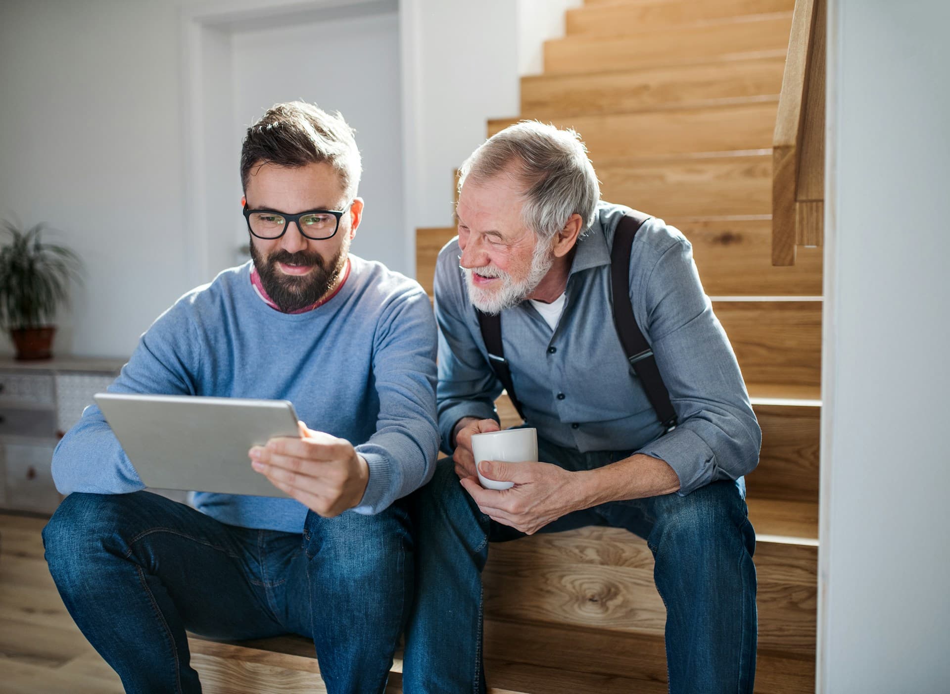 two men sitting on stairs looking at a tablet